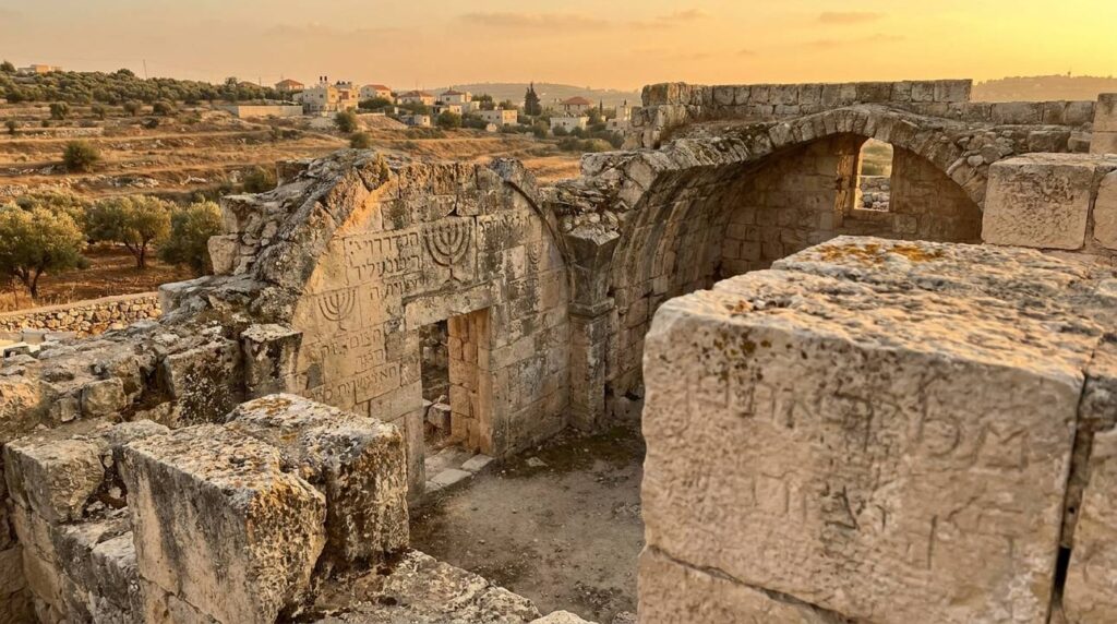 Sunset over Bethany ruins with Hebrew inscriptions and traditional symbols.